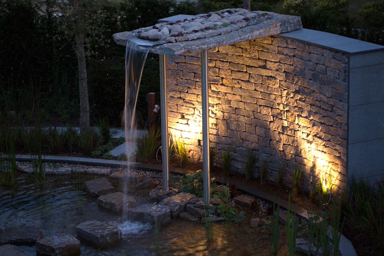 Ein Design Schwimmteich mit einer einmaligen Kombination aus runden und geradlinigen Wasserflächen an geschwungenen Natursteinmauern