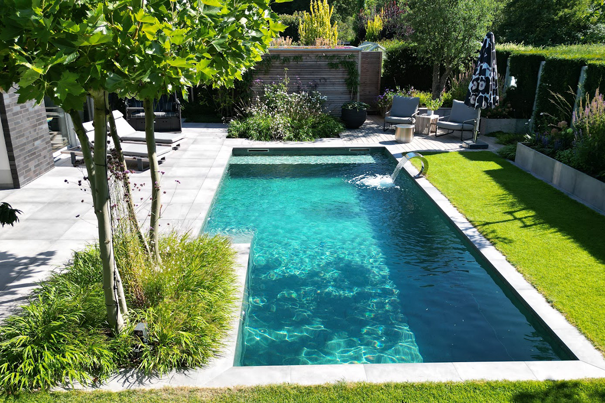 Eine sonnige Gartenlandschaft meinem einem modernen Naturstein-Pool mit einer Schwallbrause von Garten Bitters.