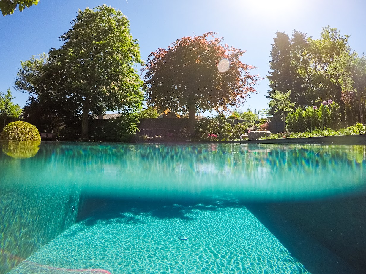 Ein Naturstein-Pool, von Garten Bitters, zur Hälfte unterwasser aufgenommen, mit Bäumen im Hintergrund.