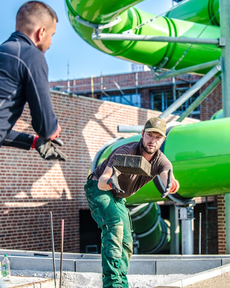 Zwei Mitarbeiter von Garten Bitters, aus dem Beriech Pflasterer, werfen sich einen Stein zu.