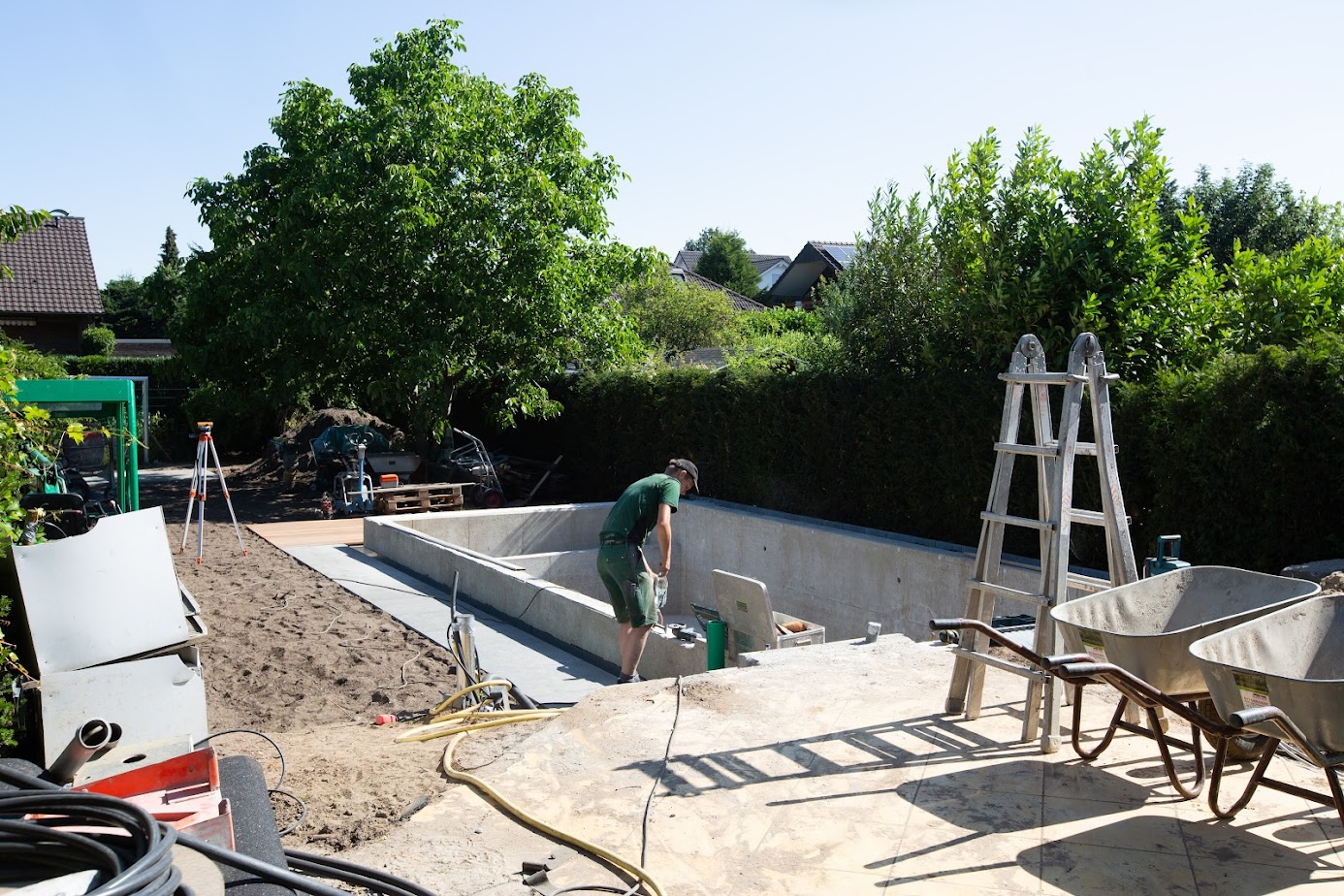 Eine aktive Pool-Baustelle von Garten Bitters mit einem Facharbeiter und einer Leiter.