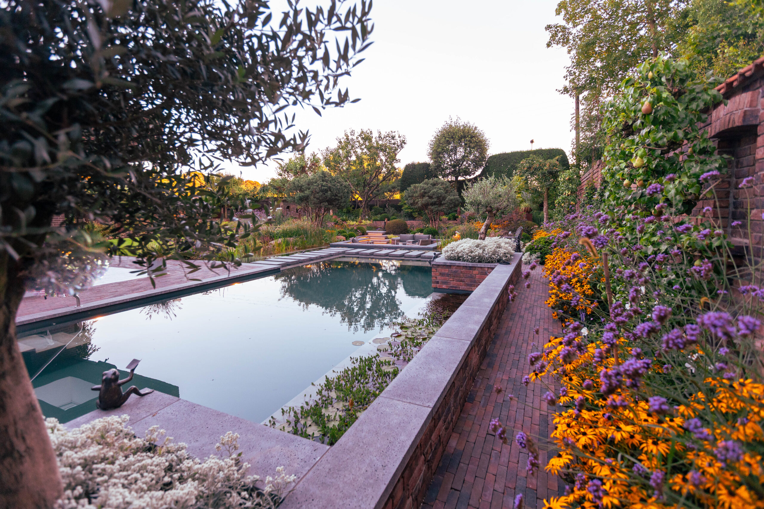 Ein Schwimmteich in einem modernen Garten von Garten Bitters mit orangenen und lila Blumen im Vordergrund.