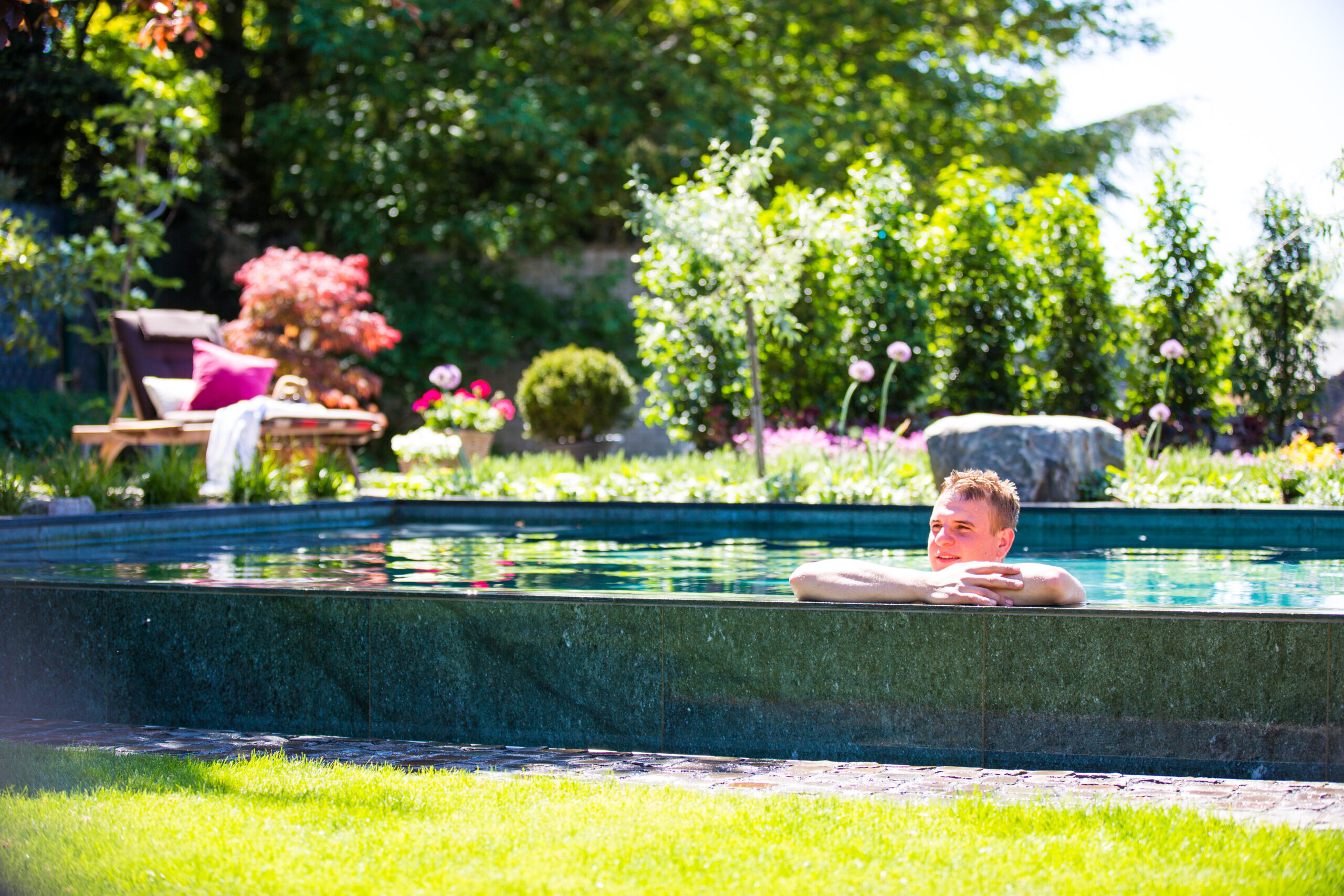 Natursteinpool mit Überlaufkante mit schwimmender Person von Garten Bitters
