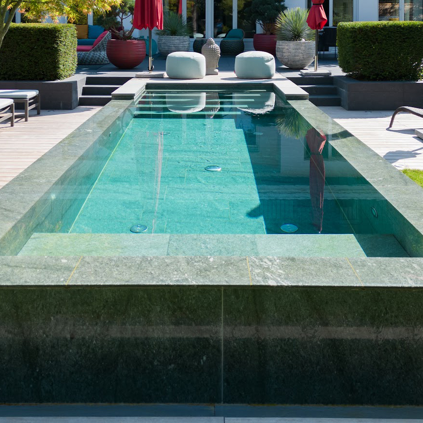 Ein Naturstein-Pool, gebaut von Garten Bitters, mit Stufen im Wasser und zwei Sitzsäcken im Hintergrund.