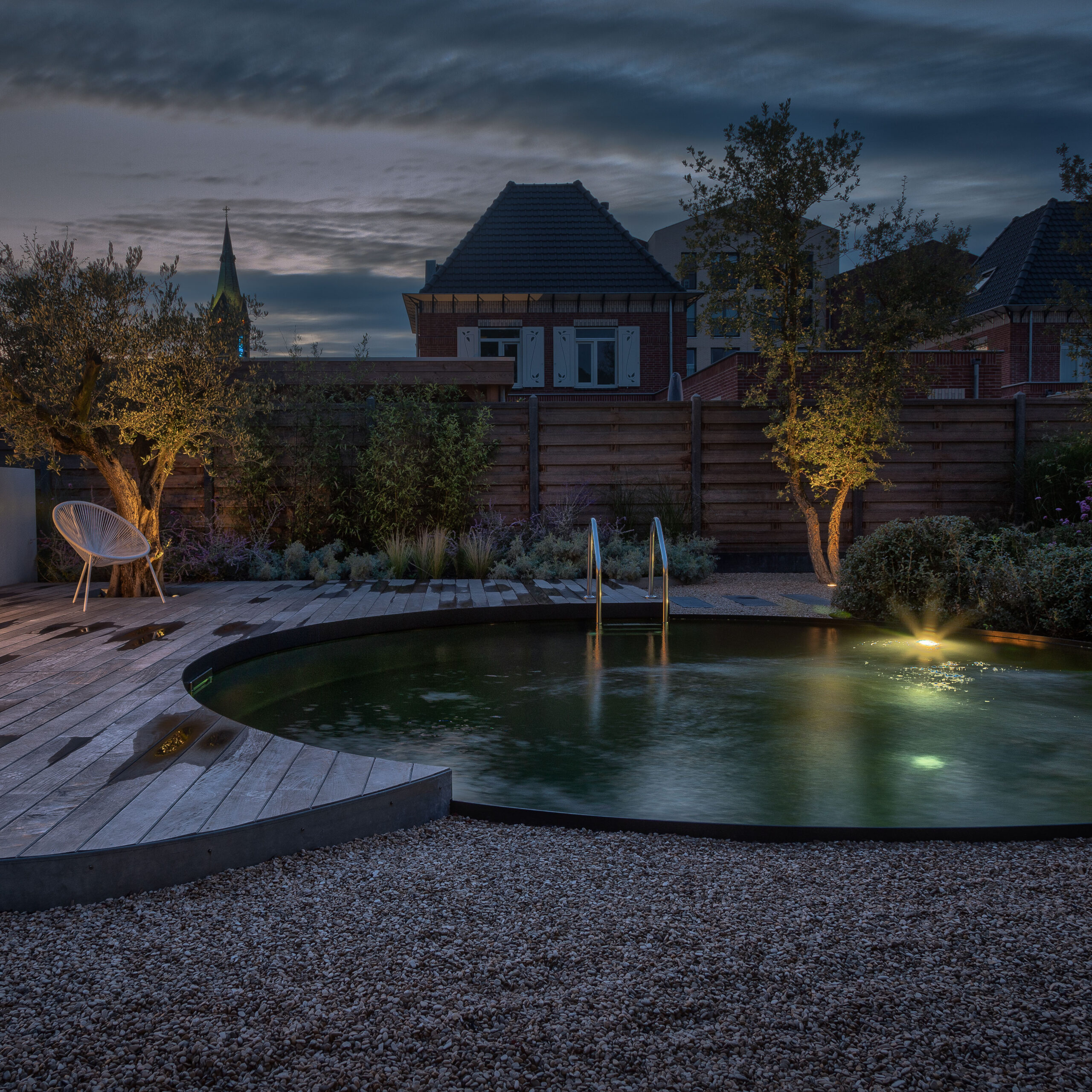 Ein runder Biotop-Living-Pool von Garten Bitters mit einer Poolleiter in der Dämmerung.