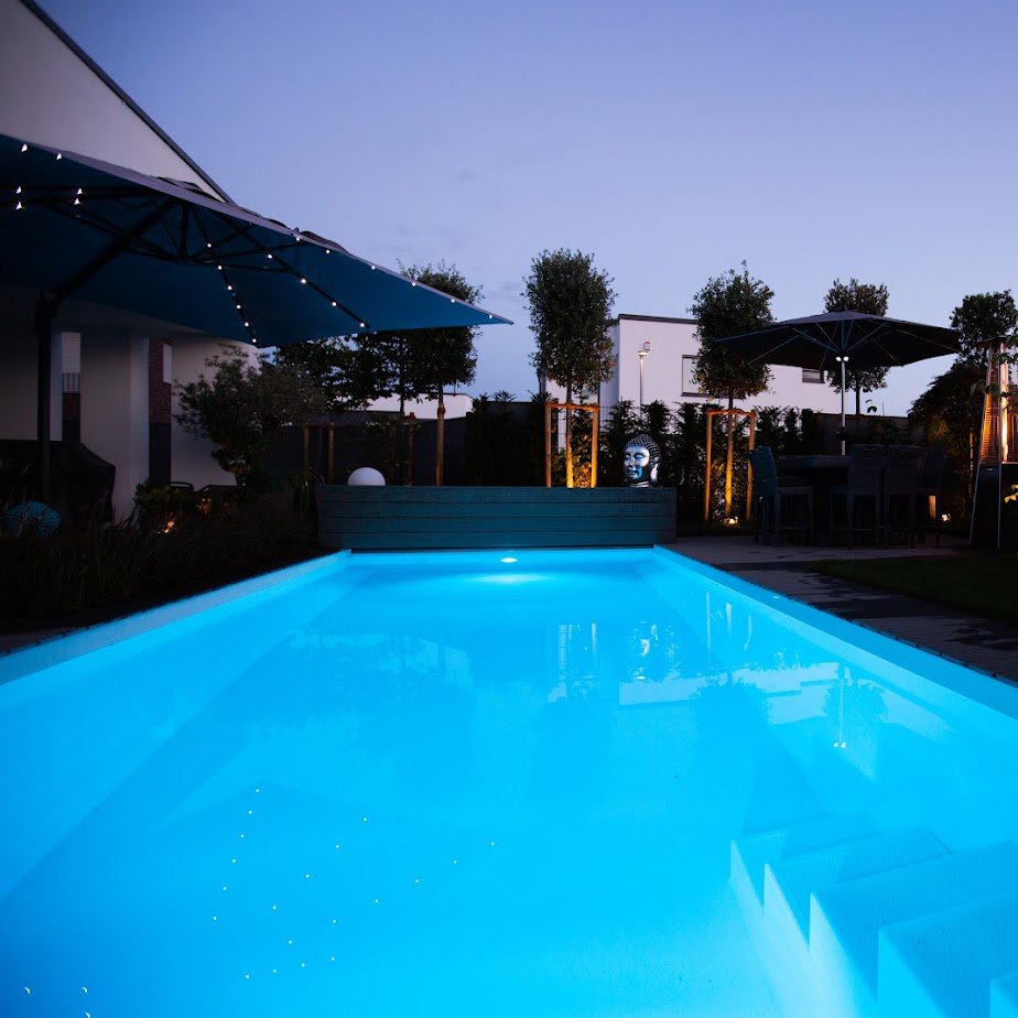 Ein Fertigbecken von Garten Bitters mit blauer Beleuchtung in der Dämmerung.