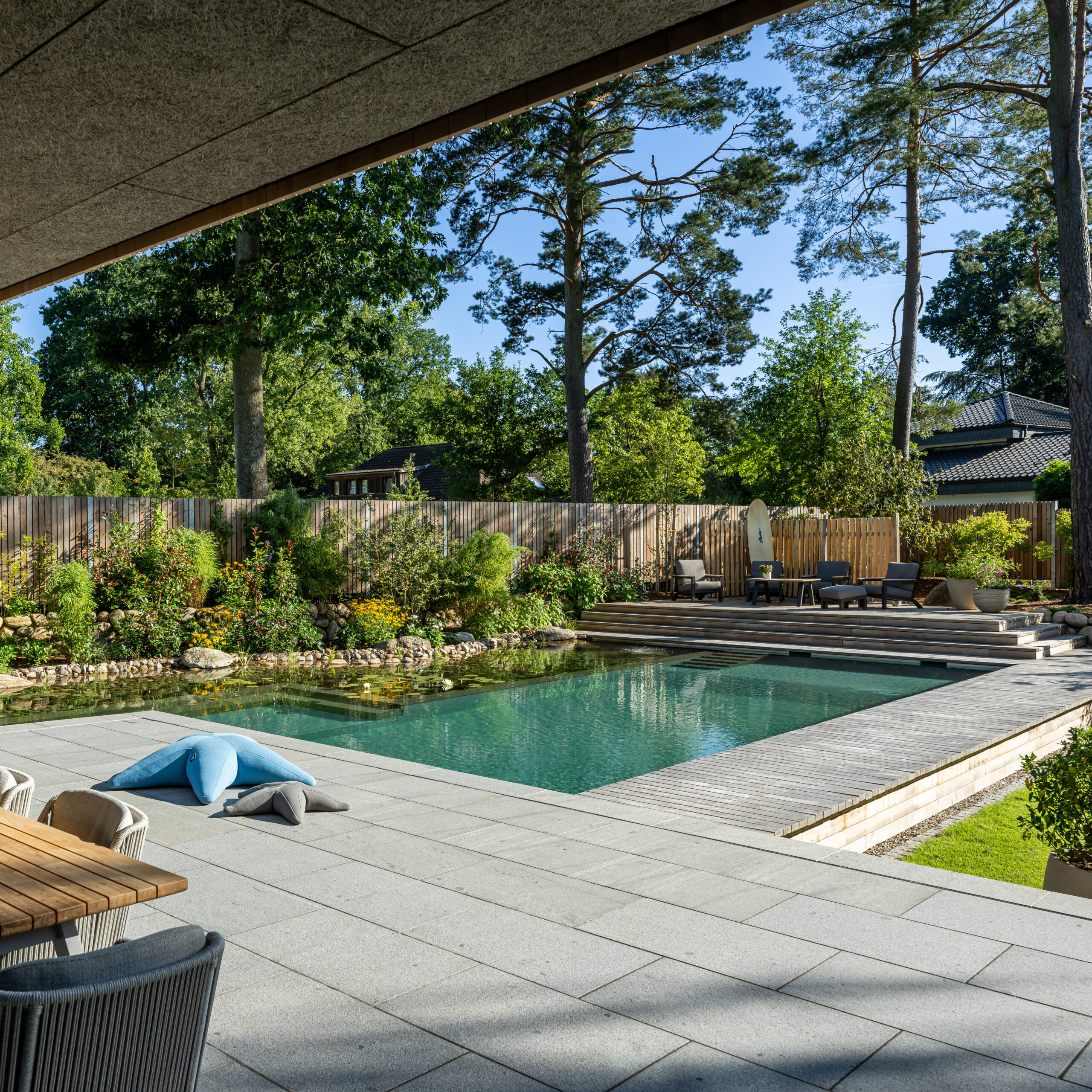 Ein Biotop-Schwimmteich mit Grünanlage, anliegend an eine Terasse.