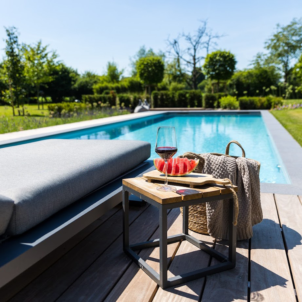 Ein Beistelltisch mit Wassermelone und Wein vor einem Folienpool von Garten Bitters.